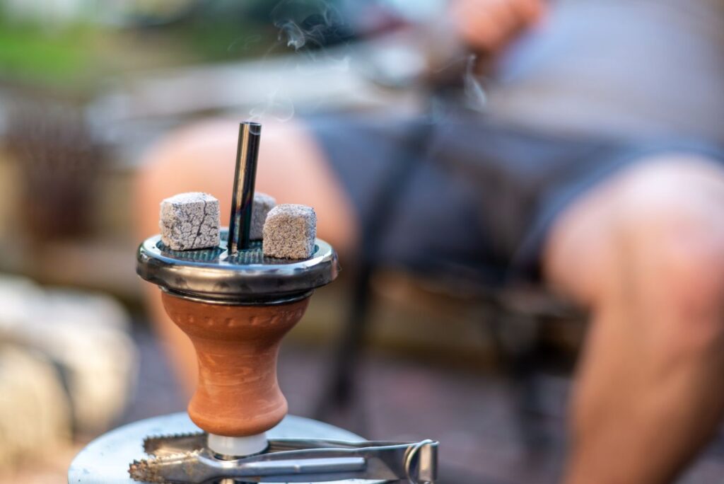 Close-up of a lit hookah with smoke and coals, capturing a casual outdoor setting.