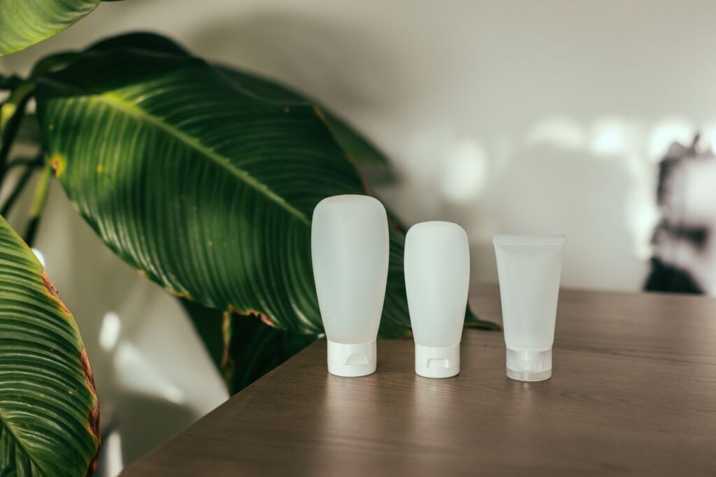 Three minimalist cosmetic bottles on a wooden table with large green leaves in the background.