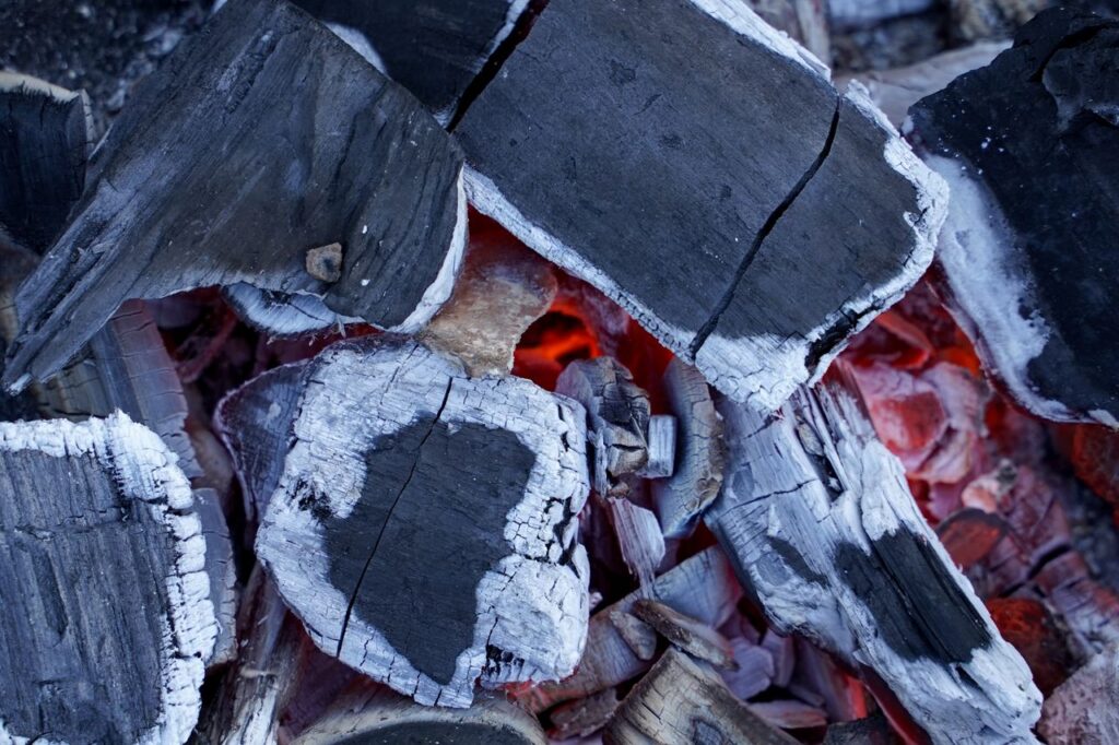 Detailed view of intense glowing charcoal embers with partially burned wood pieces.