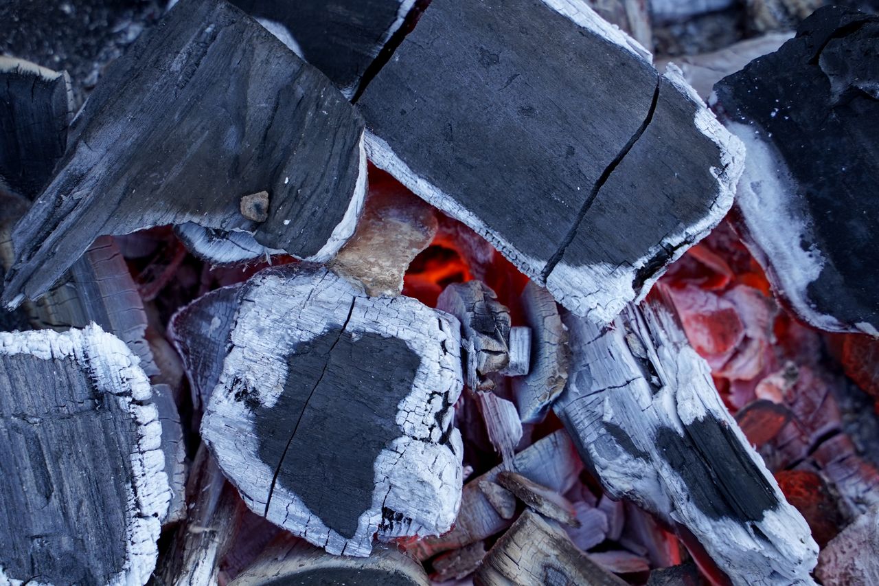 Detailed view of intense glowing charcoal embers with partially burned wood pieces.